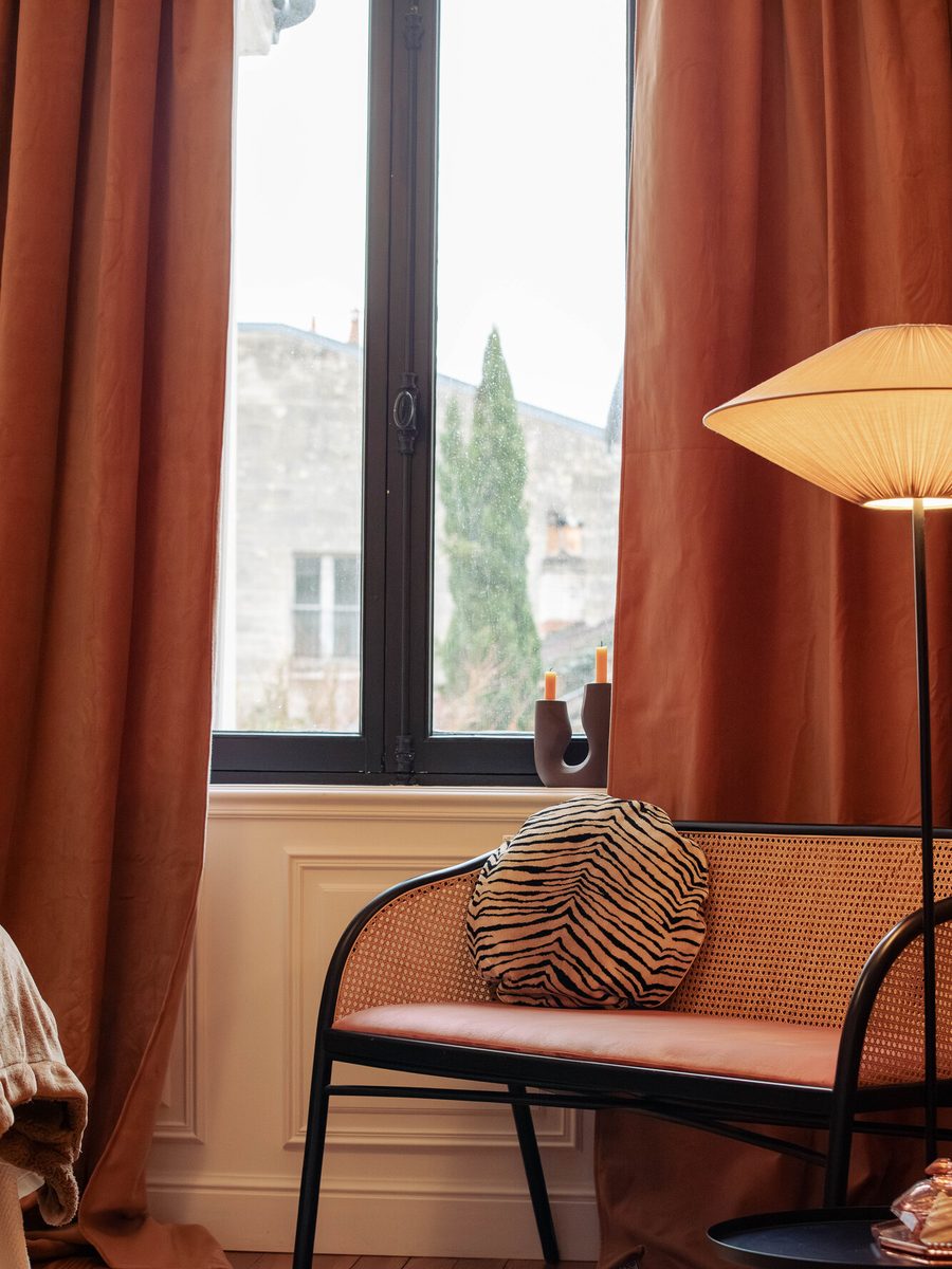 Une banquette et une fenêtre habillées de rideaux terracotta.