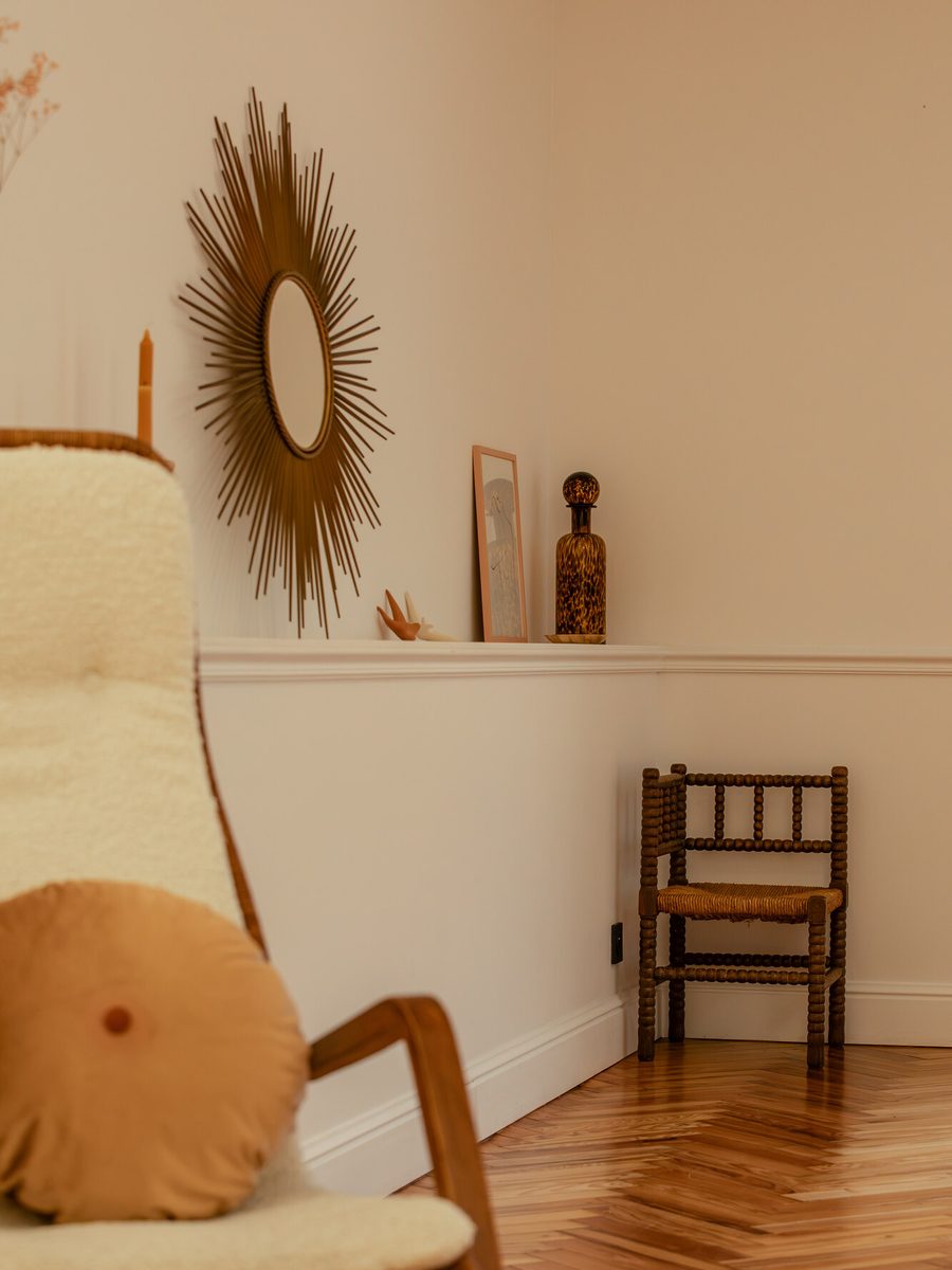 Un coin de salon, miroir soleil et fauteuil en peau de mouton.